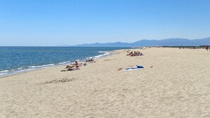 Ein weiter Sandstrand mit badenden und sonnenden Personen.
