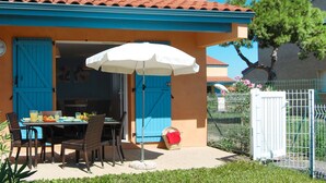 Ein Essbereich im Freien mit Tisch und Stühlen, einem weißen Sonnenschirm und einer blauen Tür.