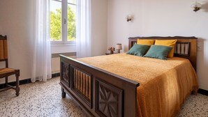 A bedroom with a wooden bed, a chair, a window with curtains, and a lamp on a bedside table. - La Vigneronne by Interhome (Fourques)