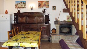 Een knusse woonkamer met een houten eettafel, stoelen, een open haard en een trap.