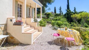 Una casa amb un porxo cobert, escales cap a una porta i un jardí amb taula i cadires.