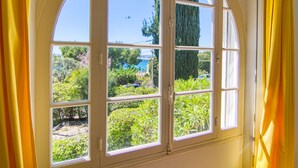 Habitació amb una gran finestra apuntada que dona a un jardí i una massa d'aigua.