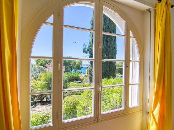 A room with a large arched window overlooking a garden and a body of water.