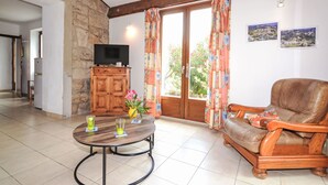 A living room with a stone wall, wooden furniture, a television on a cabinet, and a view of the outdoors through a glass door.