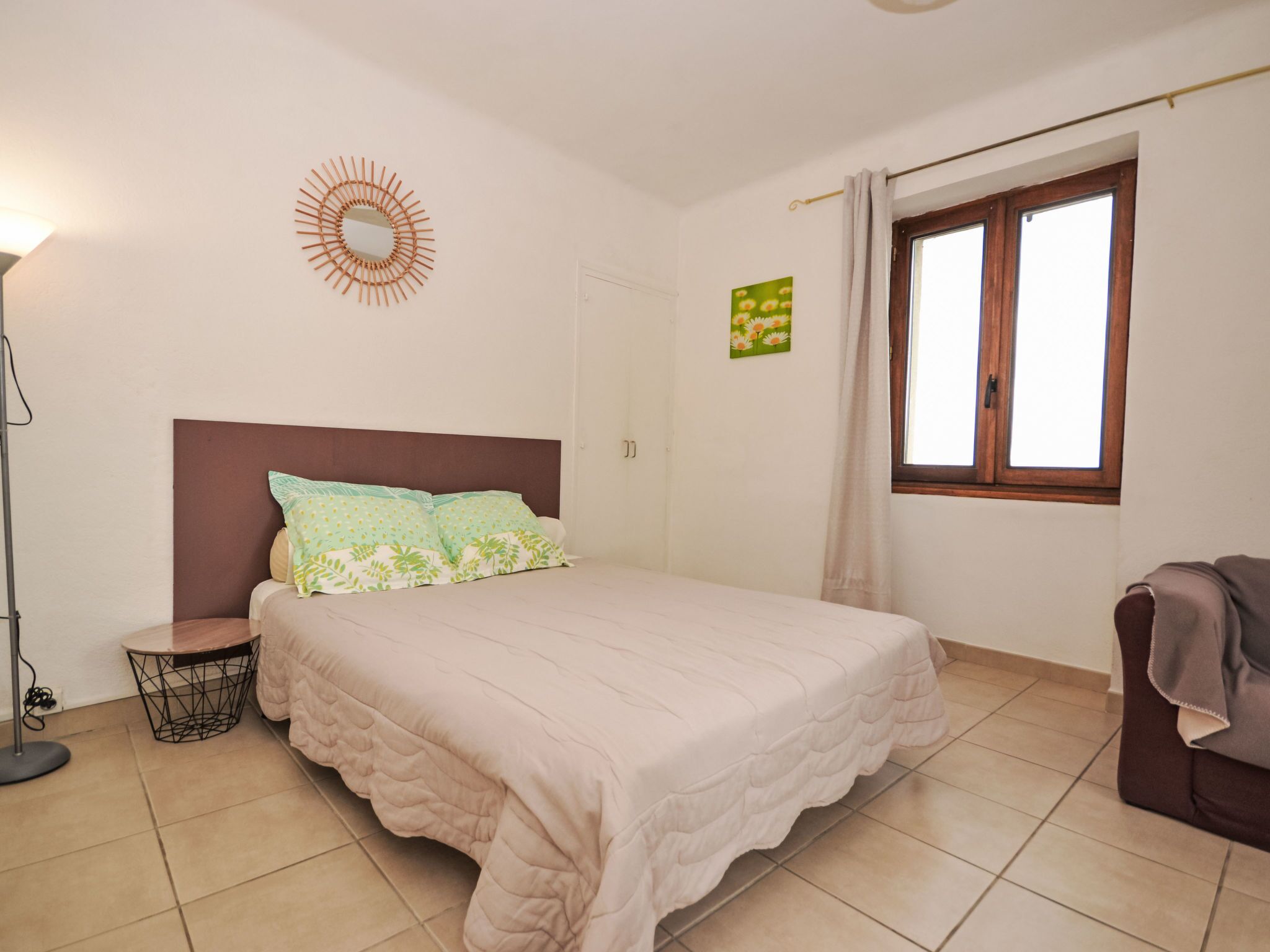 Une chambre à coucher avec un lit, une lampe sur pied, une fenêtre avec des rideaux et un élément de décoration murale.