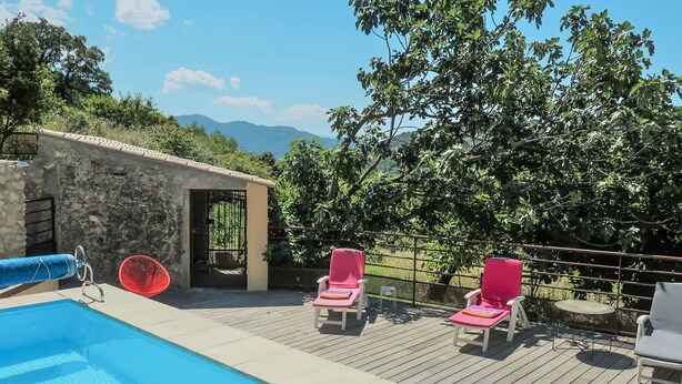 A swimming pool with two pink lounge chairs and a red chair, surrounded by a wooden deck and a stone wall. - Chaud'abri by Interhome (Nyons)