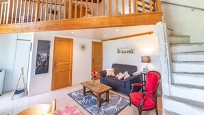 A spacious living area with a high wooden ceiling, a sofa, a red chair, a wooden table, and a staircase leading to an upper level. - Chaud'abri by Interhome (Nyons)