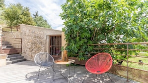 A wooden deck with two chairs, a small table, and a rustic building with a metal gate. - Chaud'abri by Interhome (Nyons)