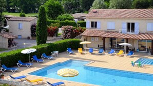 Una piscina con sillas de descanso y sombrillas, rodeada por una cerca blanca y follaje.