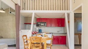 Una cocina compacta con armarios rojos, un comedor con mesa y sillas de madera, y una escalera que sube a un nivel superior.