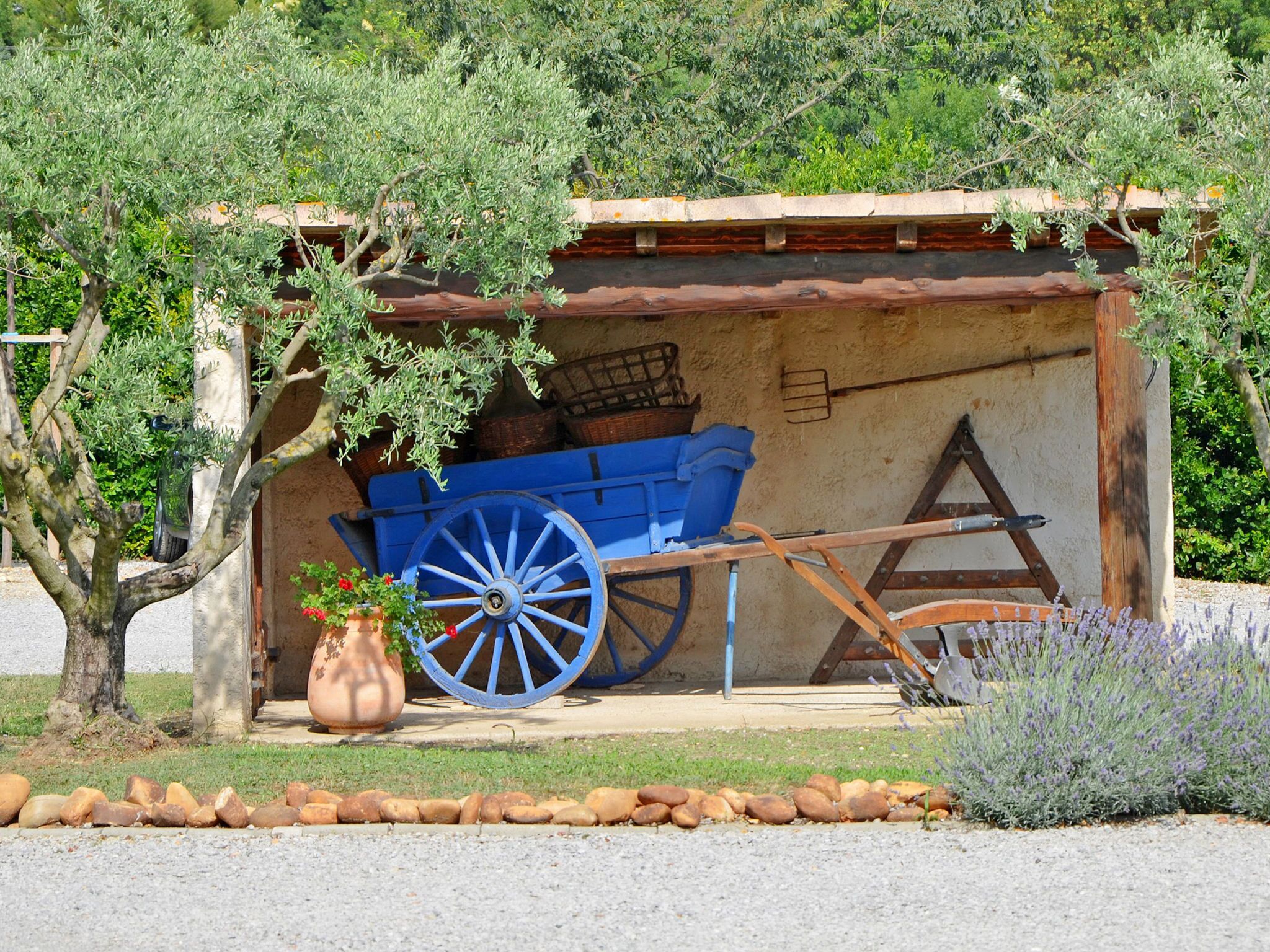 Un espacio de estar al aire libre rústico con un carro de madera azul, una maceta grande con flores y un muro de piedra.