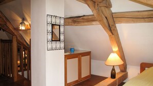 Un dormitorio con techo inclinado, vigas de madera, una mesita de noche con lámpara y un espejo en la pared.