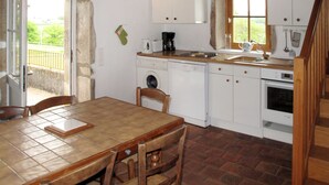 Una cocina con una mesa de baldosas, sillas de madera, lavadora, estufa y ventana con vistas a zonas verdes.