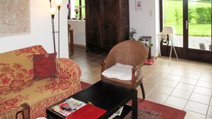 Un salon comprenant un canapé, un fauteuil en osier, une table basse et une vue sur un jardin, visible à travers une porte vitrée.