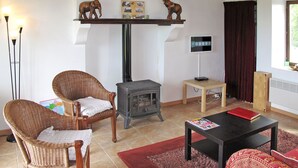 Un salon avec une cheminée, deux fauteuils en osier, une table basse et un téléviseur posé sur un meuble.