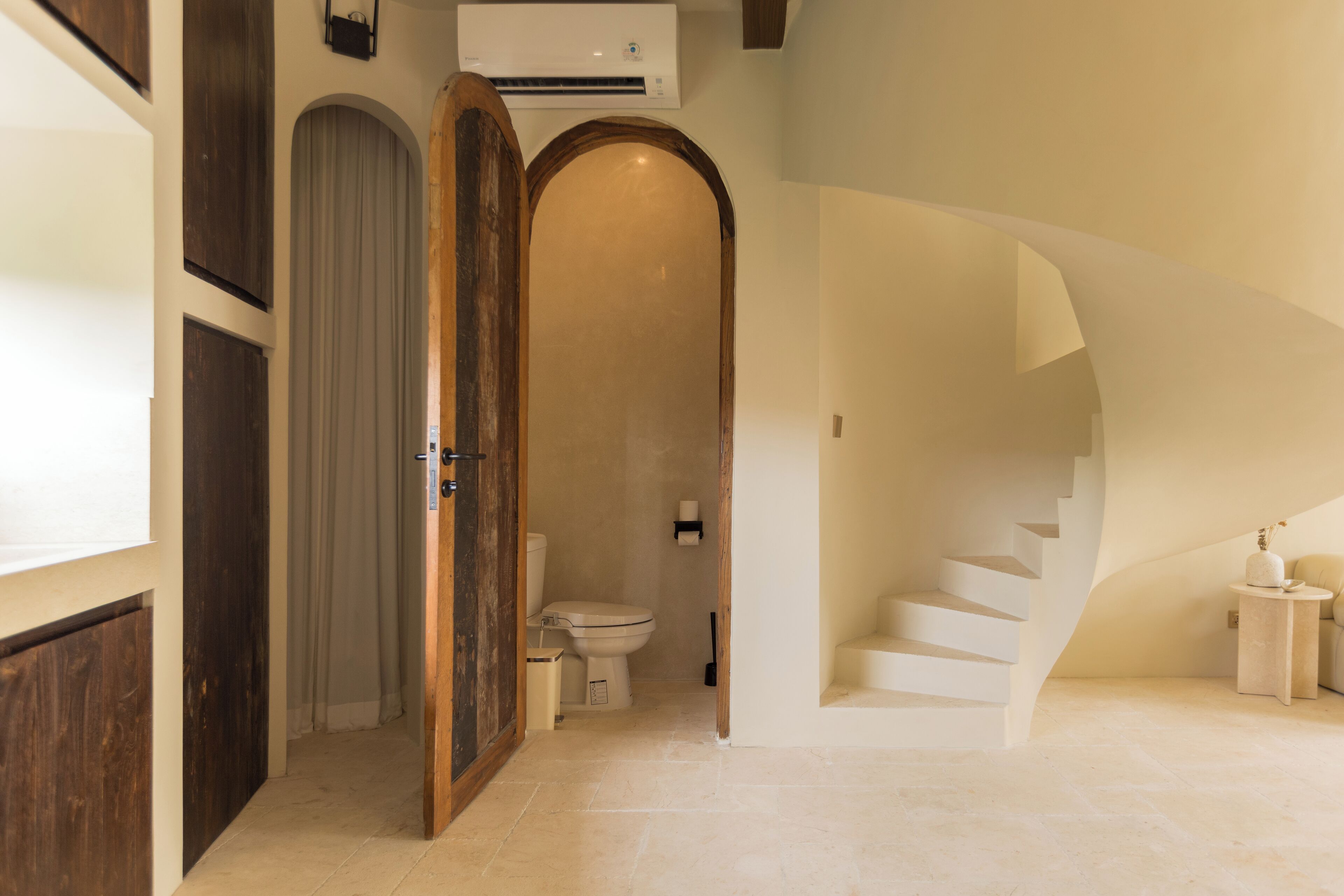 Un interior moderno con una puerta de madera, un inodoro blanco y una escalera de caracol.