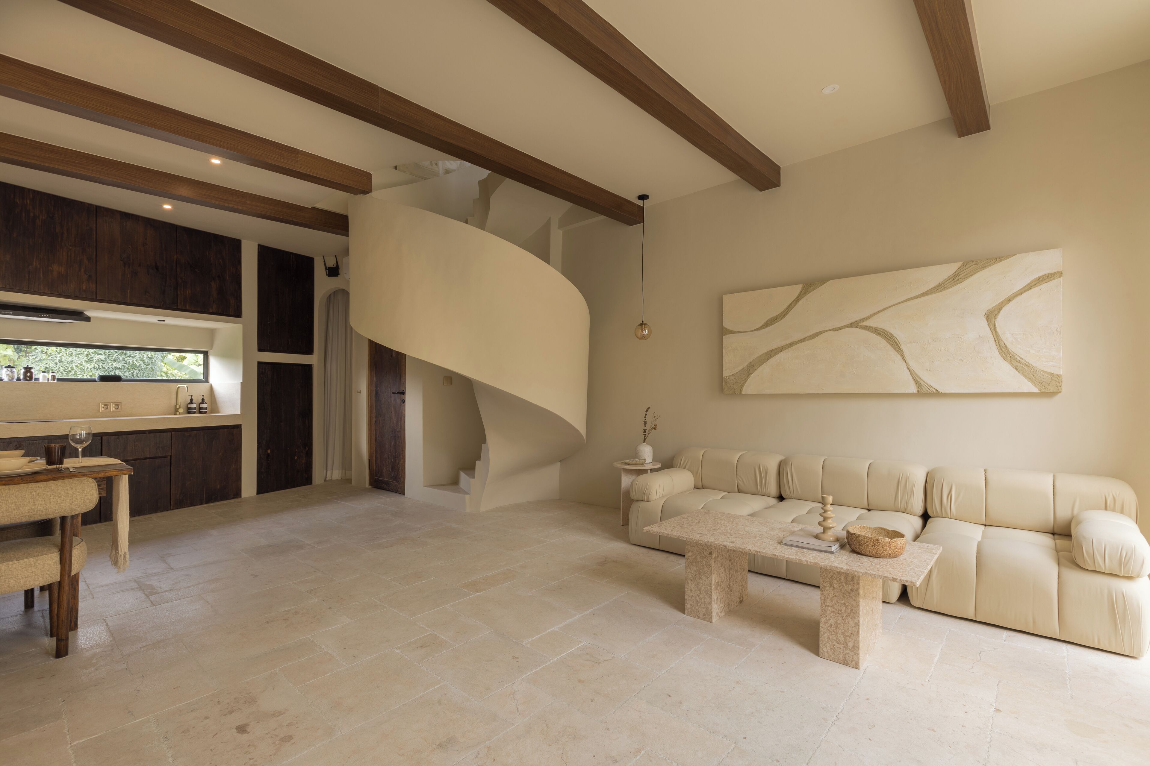 Un interior moderno con una escalera curva, un sofá color beige y un comedor con una mesa y sillas.