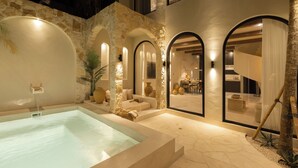 A modern outdoor pool area with stone walls and arched openings, a hot tub, and a seating area with cushions. - Romantic Tropical Villa Sawa  Pererenan (Canggu)