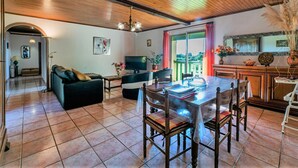 A spacious living room with a wooden ceiling, a dining area with a glass table, and a kitchen visible through an open door. - Le Coustal by Interhome (Blanquefort-sur-Briolance)