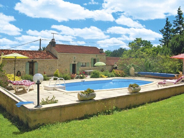 Une maison en pierre avec une piscine, un espace salon extérieur et un jardin.
