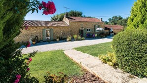 A stone house with a tiled roof, a gravel driveway, and a well-maintained garden with various plants and flowers. - Le Coustal by Interhome (Blanquefort-sur-Briolance)