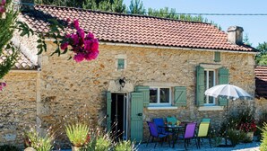 A stone building with a tiled roof, a door, and a window with shutters. There is a table with chairs and a potted plant in front. - Le Coustal by Interhome (Blanquefort-sur-Briolance)