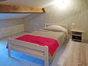 Una cama individual con una manta roja en una habitación con techo inclinado y vigas de madera.