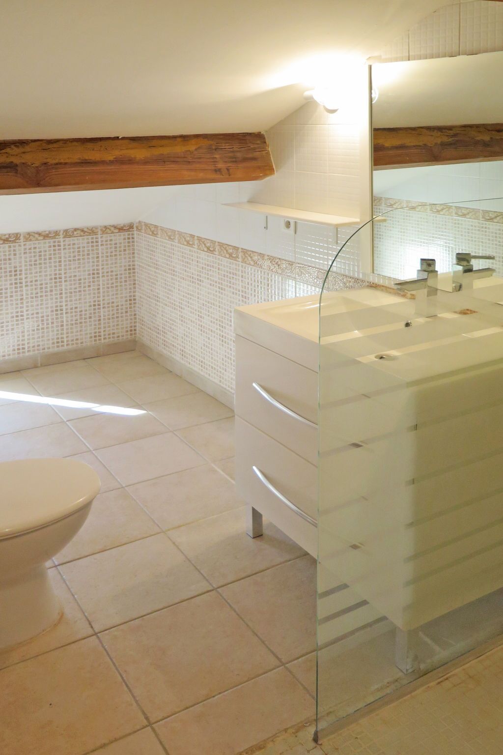 A bathroom with a glass-enclosed sink, a toilet, and a tiled floor.