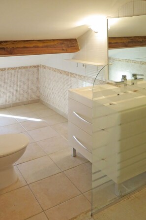 Un baño con lavamanos de cristal, inodoro y piso de baldosas.