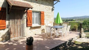A stone building with a patio area featuring a table and chairs, a green umbrella, and a view of the countryside. - Sarrouil by Interhome (Loubressac)