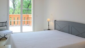 Ein Schlafzimmer mit einem Bett, einem Nachttisch, einer Lampe, einem Stuhl und einer Glasglastür, die zu einem Außenbereich mit Holzzaun führt.