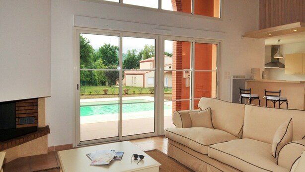 Ein geräumiges Wohnzimmer mit großen Glasschiebetüren zum Poolbereich, einem beigen Sofa, einem kleinen Couchtisch und einem Kamin.