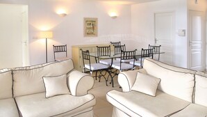 Ein Wohnzimmer mit zwei hellbeigen Sofas, einem Esstisch mit Glasplatte und Stühlen sowie einem kleinen Gemälde an der Wand.
