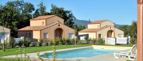 A residential area with two houses, a swimming pool, and a fenced garden.