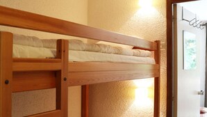 A bunk bed with a wooden frame and white bedding, located in a room with a wooden floor and a door in the background. - Fully-equipped studio for 4 people (LES ORRES 1650)