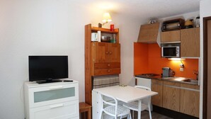 A compact kitchenette with a microwave, stove, and sink. There's a small dining table with chairs and a television on a cabinet. - Fully-equipped studio for 4 people (LES ORRES 1650)