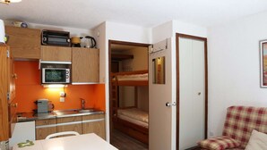 A compact room with a kitchenette, a bunk bed, and a plaid chair. - Fully-equipped studio for 4 people (LES ORRES 1650)