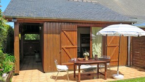 A wooden building with a tiled roof, a patio with a table and chairs, and an umbrella.