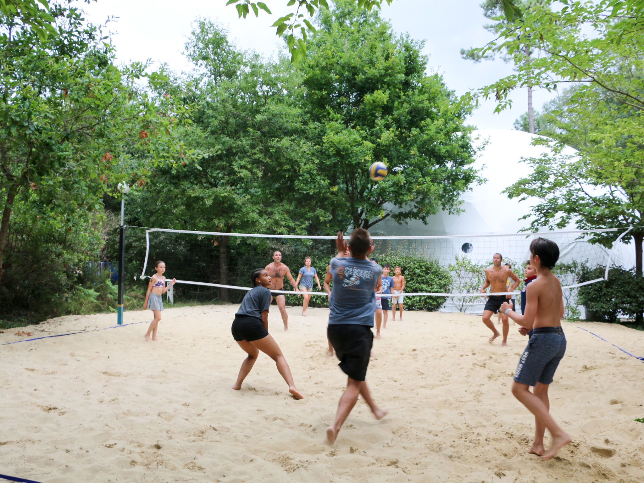 En strandvolleybollmatch på en sandplan omgiven av träd.