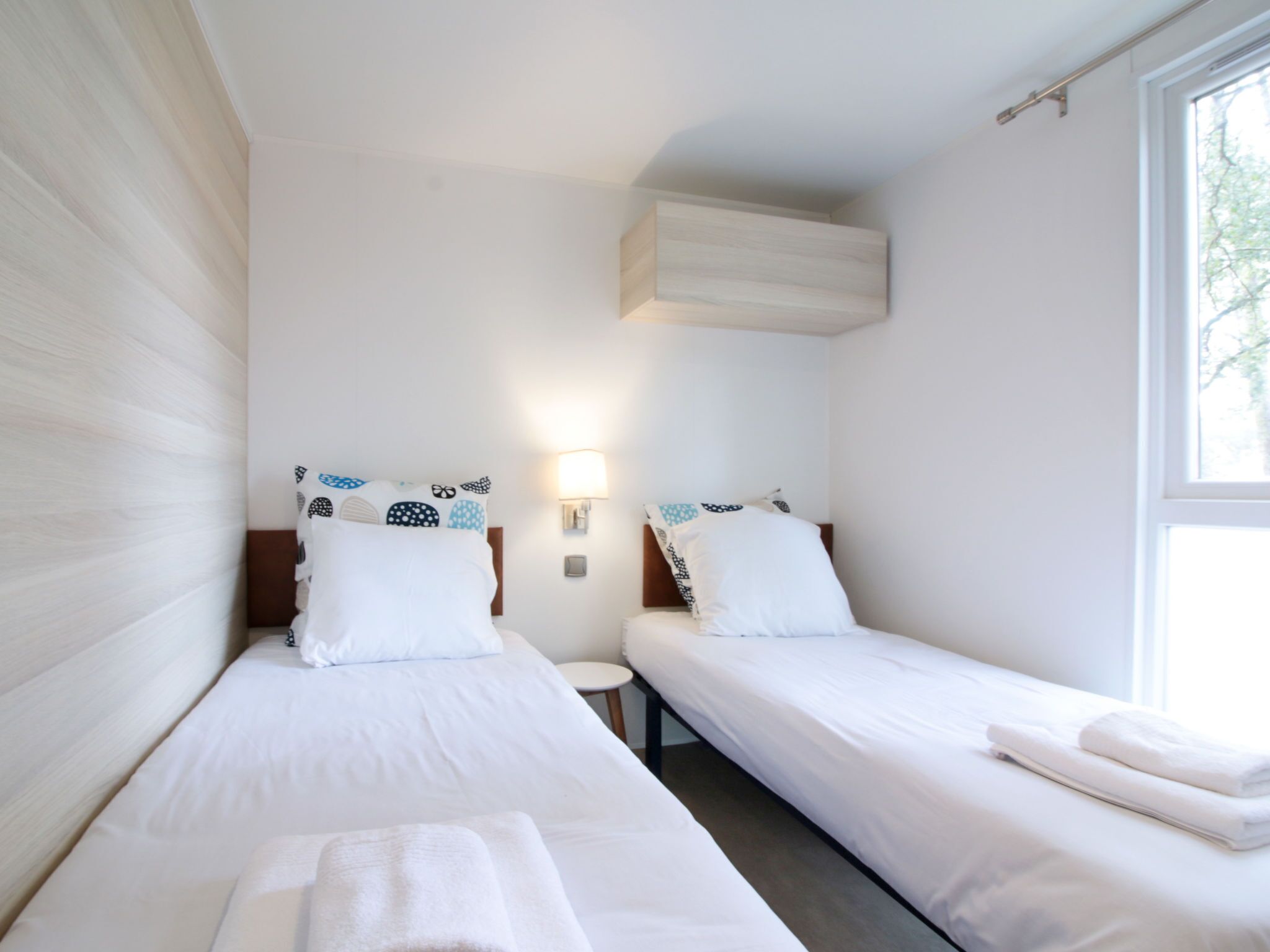 Une chambre d’hôtel avec deux lits simples, une petite table de chevet, une lampe fixée au mur et une fenêtre.