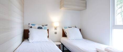 Une chambre d’hôtel avec deux lits simples, une petite table de chevet, une lampe fixée au mur et une fenêtre.