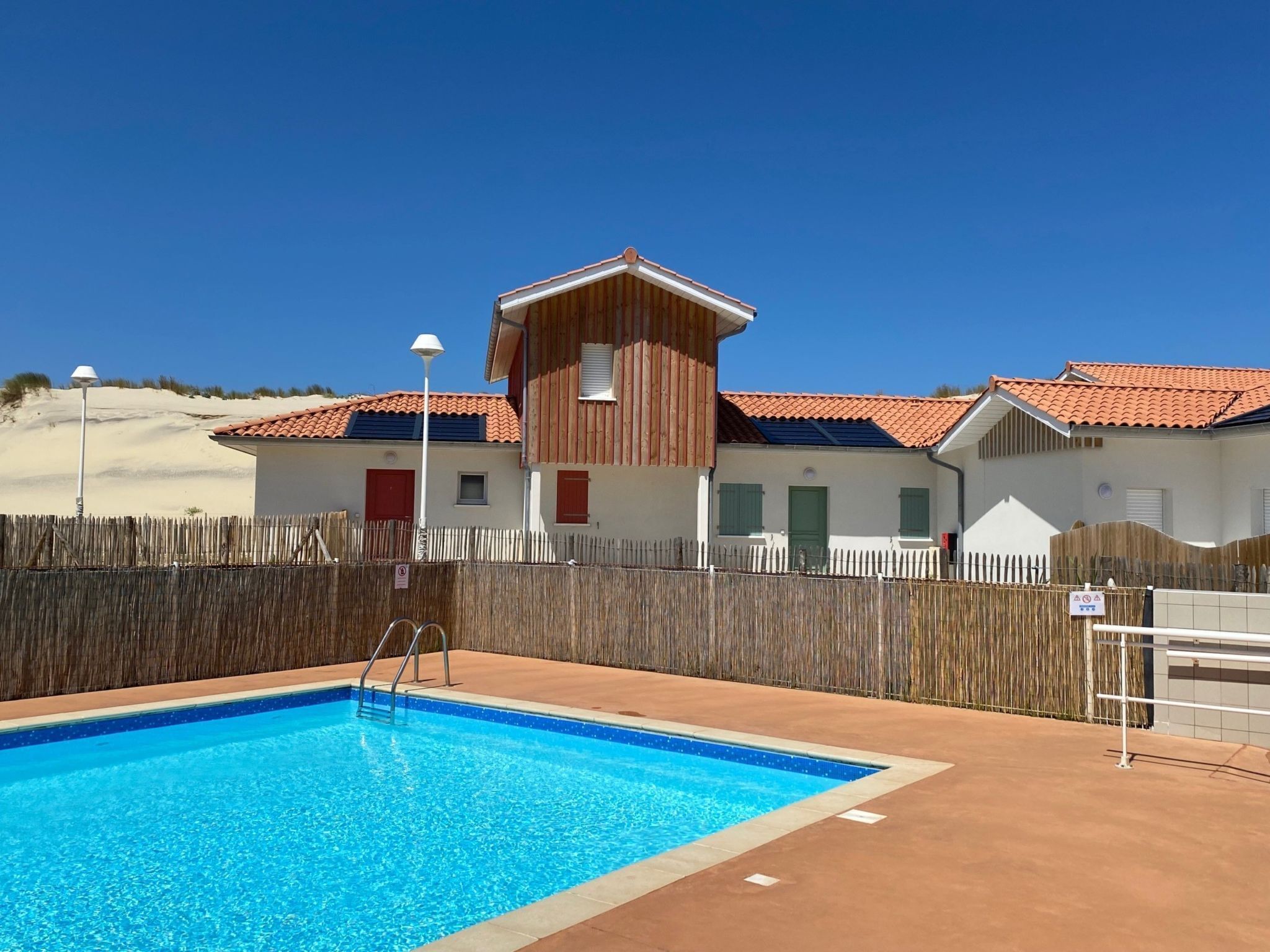 Una piscina con muelle de madera y un edificio con puertas y ventanas rojas.