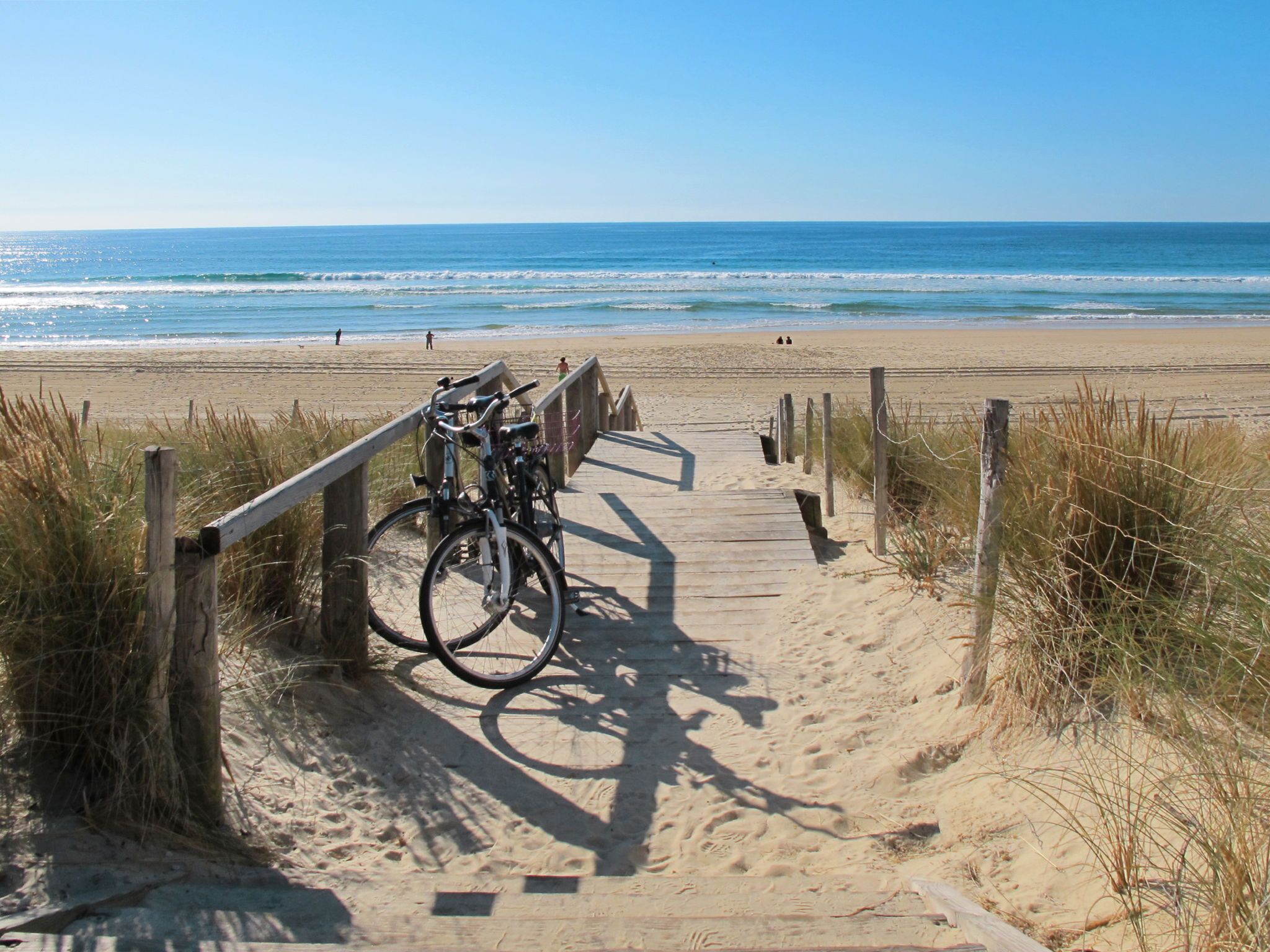 A wooden boardwalk leading to a beach with bicycles parked along the path.