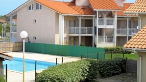 A multi-story hotel with balconies, a swimming pool, and a green fence.