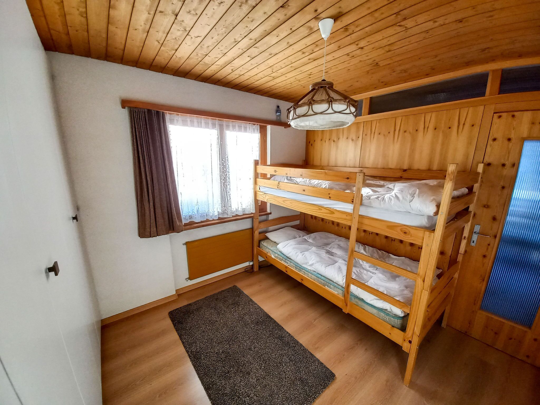 Ein Schlafraum mit Etagenbetten, Holzboden, einem Fenster mit Vorhängen und einem Heizkörper.