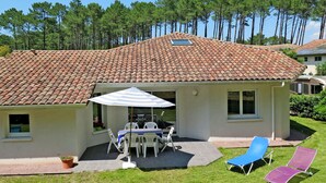 A house with a tiled roof, a patio with a table and chairs, and two lounge chairs. - Le Moïsan by Interhome (Messanges)