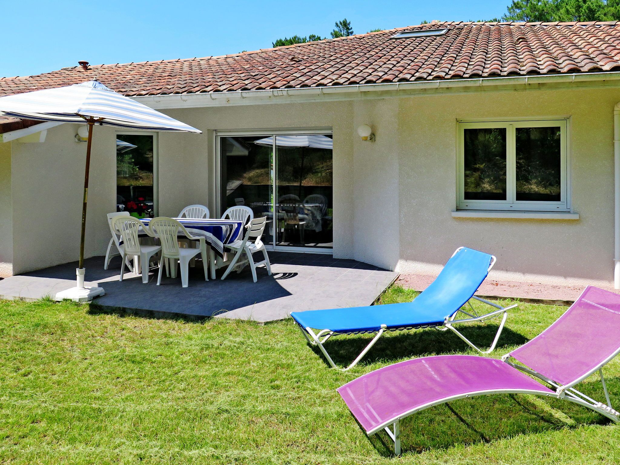 A patio with a table and chairs, a blue and white striped umbrella, and two lounge chairs.