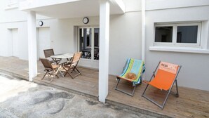 Ein überdachter Außenbereich mit Tisch und Stühlen, einem kleinen Fenster und einer Tür, die auf einen Balkon führt.