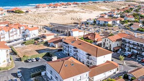 Ein Küstenwohngebiet mit Häusern und roten Ziegeldächern, ein Strand im Hintergrund und ein klarer Himmel.