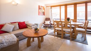 A modern living room with a sofa, a round wooden table, and a dining area with chairs.